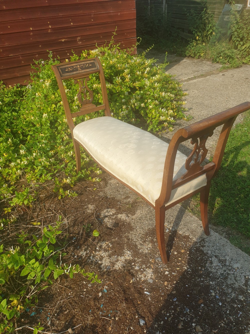 An antique wooden window seat featuring raised ends with lyre-carved splats, floral marquetry top rails, and a cream patterned upholstered cushion. View VI