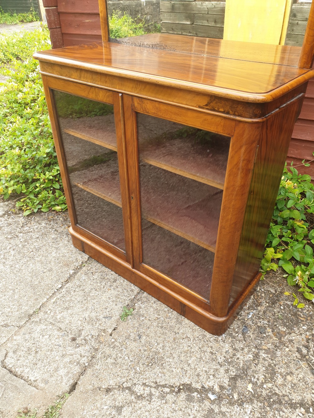 A Victorian warm brown walnut drinks cabinet featuring two glazed doors, internal wooden shelving, and an arched mirror frame topped with a carved cresting. View II