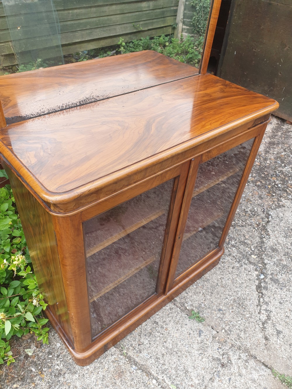 A Victorian warm brown walnut drinks cabinet featuring two glazed doors, internal wooden shelving, and an arched mirror frame topped with a carved cresting. View III