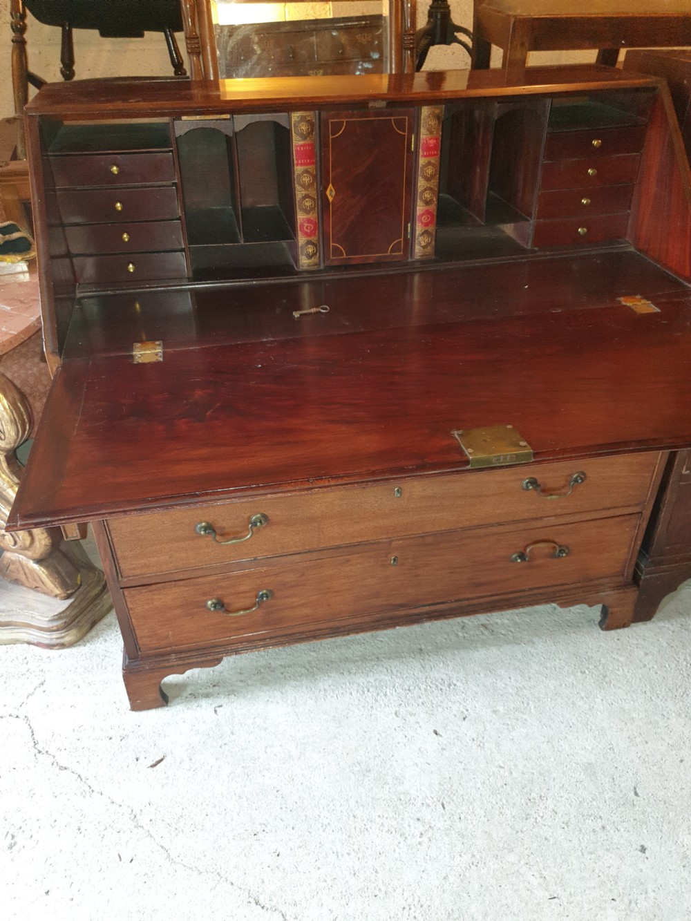 An early 19th century mahogany slant-front bureau featuring a fitted interior with small drawers and pigeonholes above two wide lower drawers with brass handles.