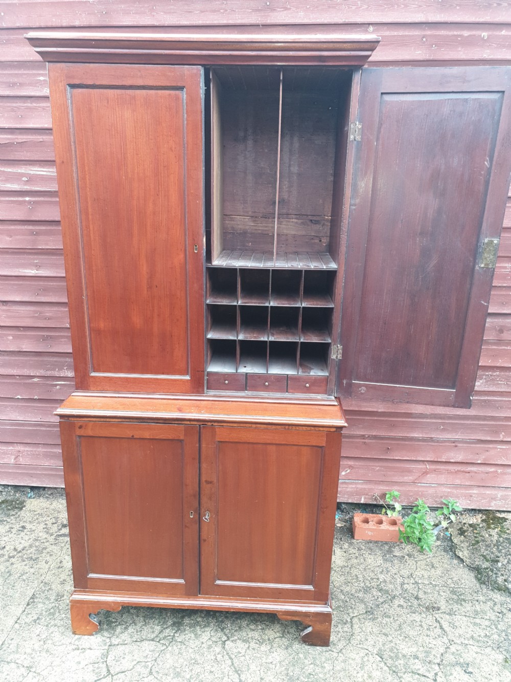 An early nineteenth-century mahogany fitted office cabinet featuring upper panel doors opening to internal pigeonholes and vertical dividers, above lower double cupboard doors on bracket feet.