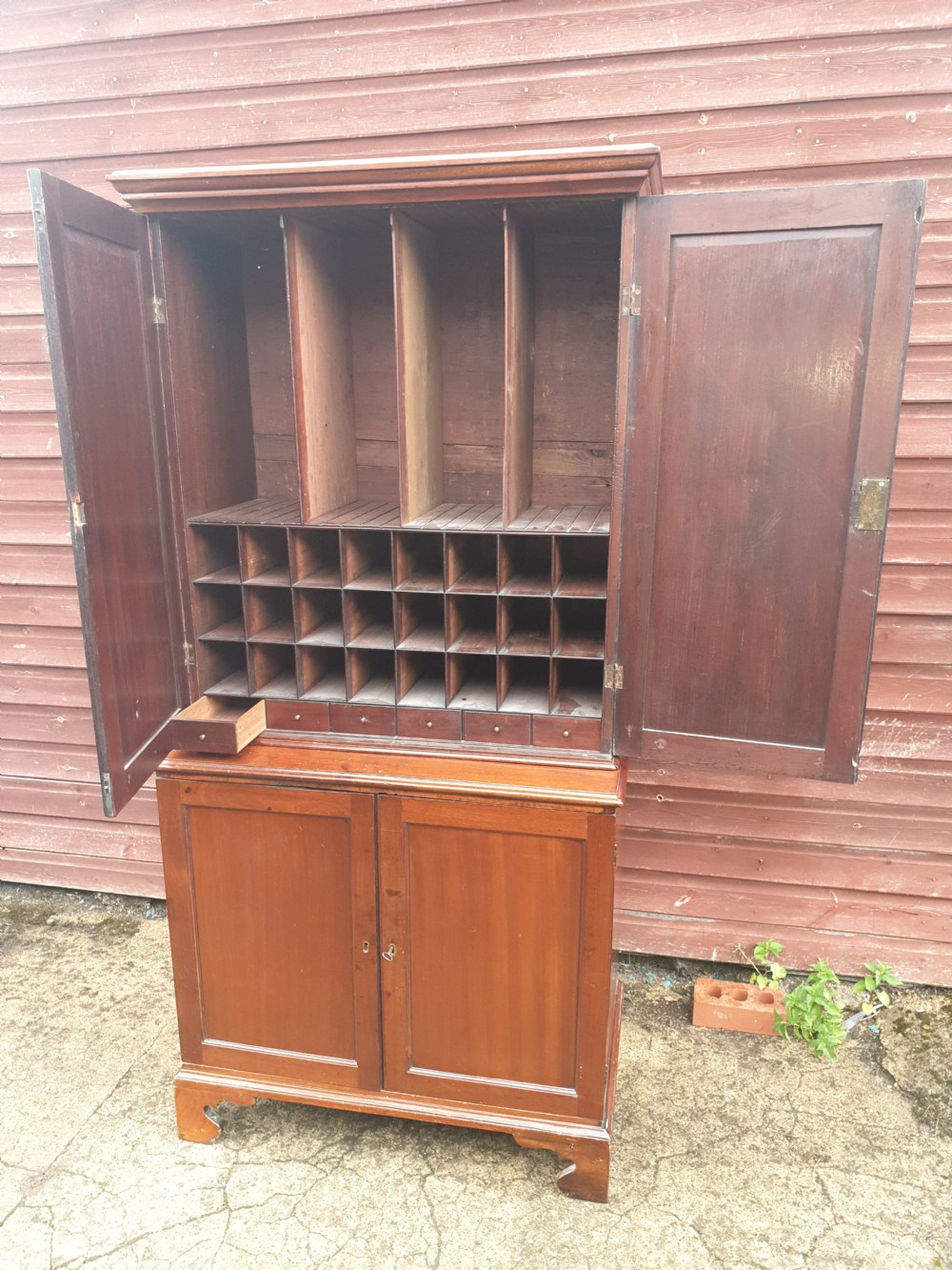 An early nineteenth-century mahogany fitted office cabinet featuring upper panel doors opening to internal pigeonholes and vertical dividers, above lower double cupboard doors on bracket feet. View II