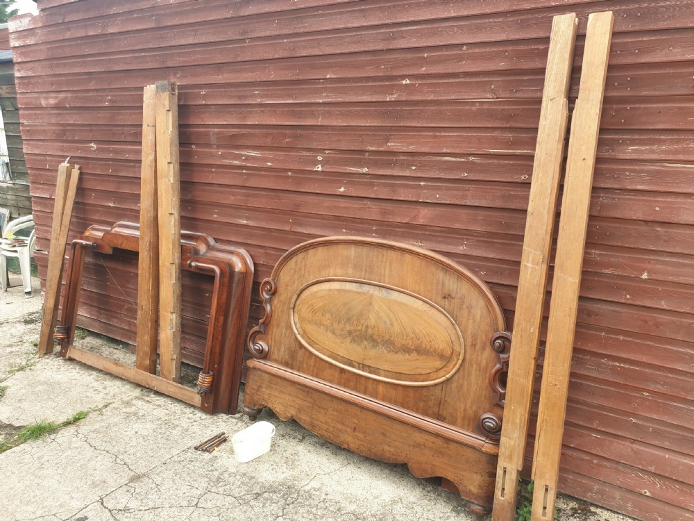 Dismantled mid-19th century mahogany half tester bed showing arched flame mahogany headboard, scroll carvings, side rails, and canopy timber framing.