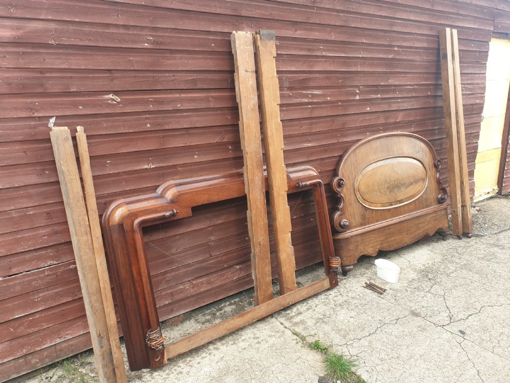 Dismantled mid-19th century mahogany half tester bed showing arched flame mahogany headboard, scroll carvings, side rails, and canopy timber framing. View II