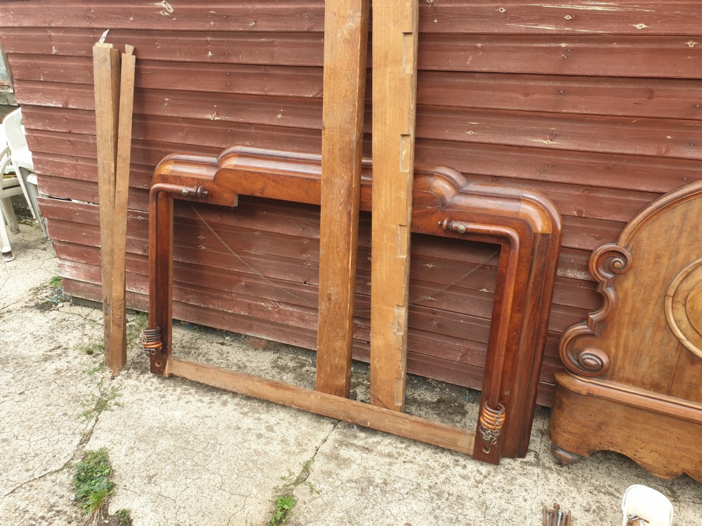 Dismantled mid-19th century mahogany half tester bed showing arched flame mahogany headboard, scroll carvings, side rails, and canopy timber framing. View V