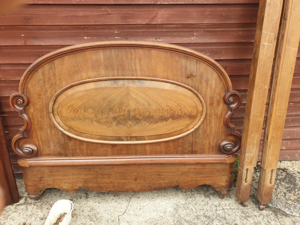 Dismantled mid-19th century mahogany half tester bed showing arched flame mahogany headboard, scroll carvings, side rails, and canopy timber framing. View VI