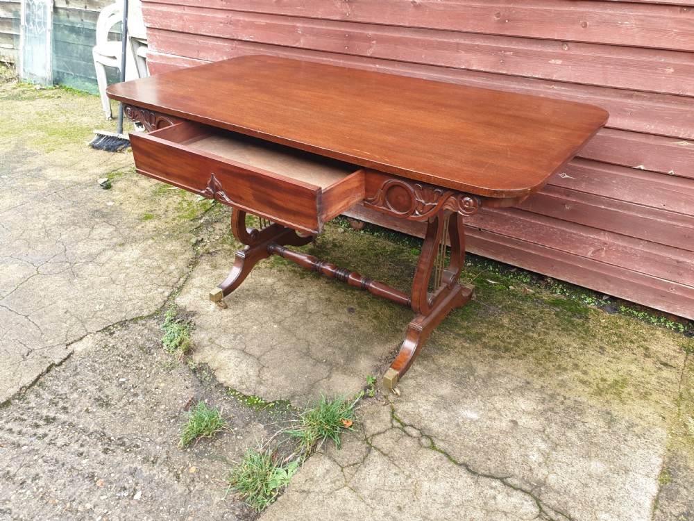A 19th-century mahogany side table with an open single drawer, carved scroll frieze, lyre end supports, and brass castors.