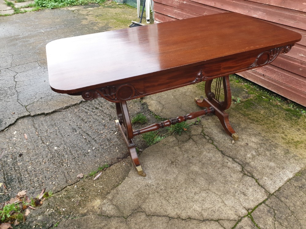A 19th-century mahogany side table with an open single drawer, carved scroll frieze, lyre end supports, and brass castors. View VI