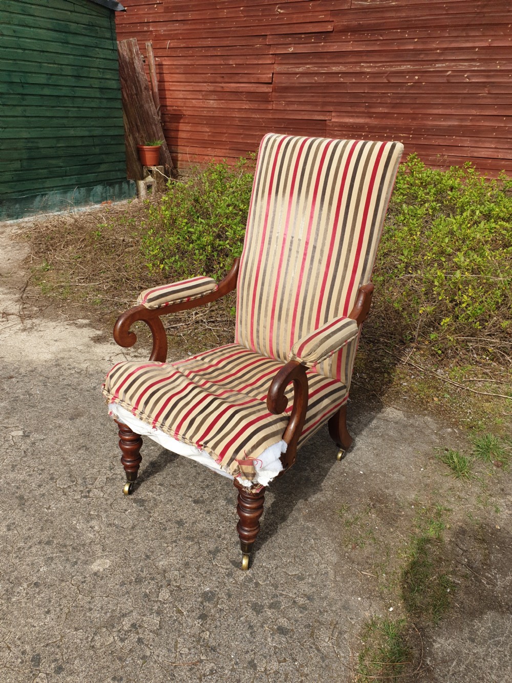 A Regency period mahogany armchair featuring a high backrest, padded scroll arms, striped fabric upholstery, and turned front legs on brass castors.