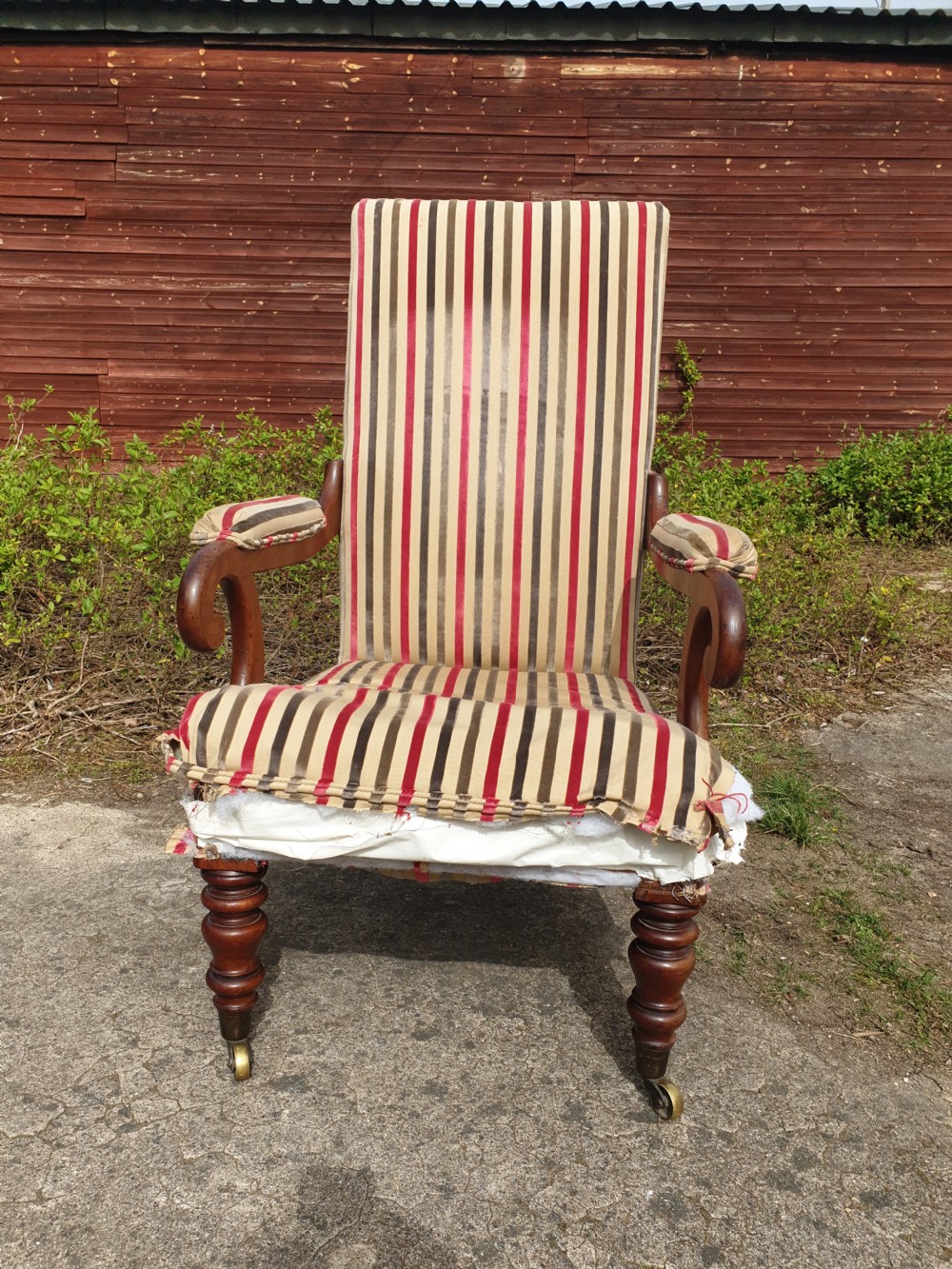 A Regency period mahogany armchair featuring a high backrest, padded scroll arms, striped fabric upholstery, and turned front legs on brass castors. View II