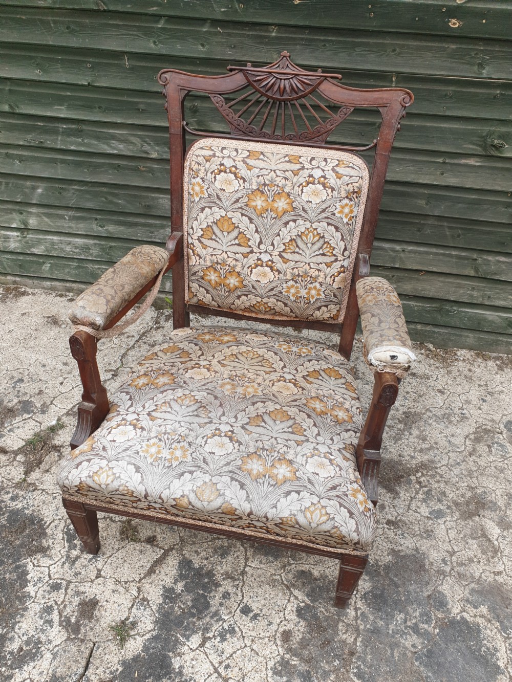 A late Victorian mahogany armchair featuring a carved openwork sunburst cresting rail, upholstered back panel and seat in a floral pattern, and padded armrests.