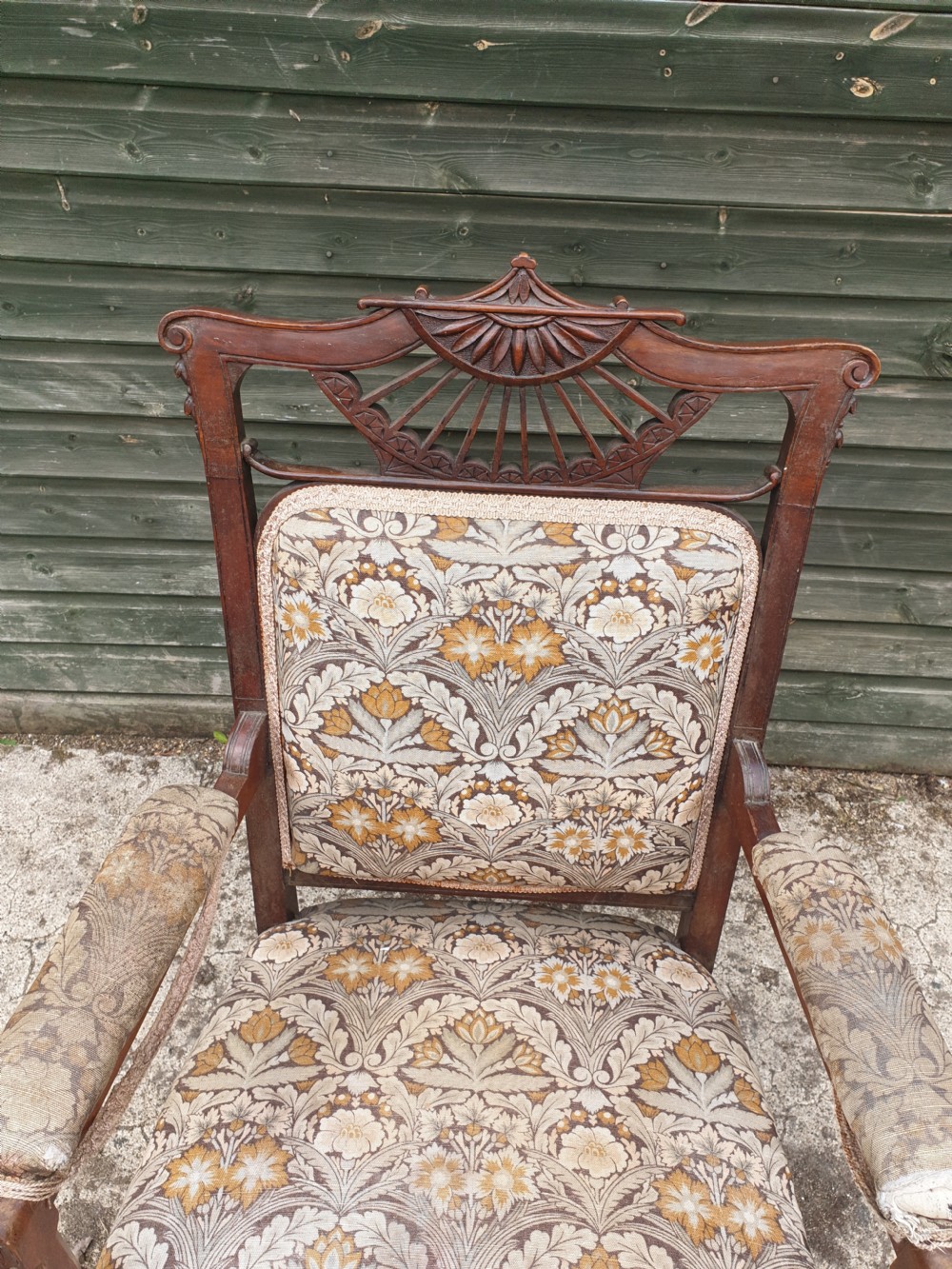 A late Victorian mahogany armchair featuring a carved openwork sunburst cresting rail, upholstered back panel and seat in a floral pattern, and padded armrests. View II