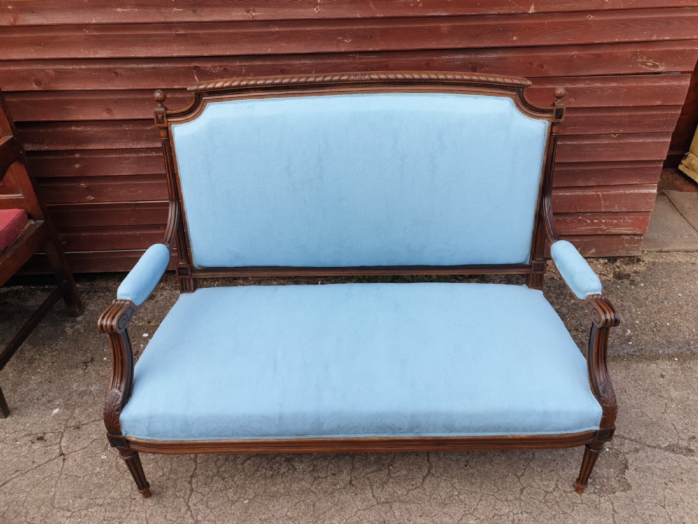 A French walnut two-seater hall settee featuring a carved wooden frame, fluted legs, padded armrests, and light blue upholstery.