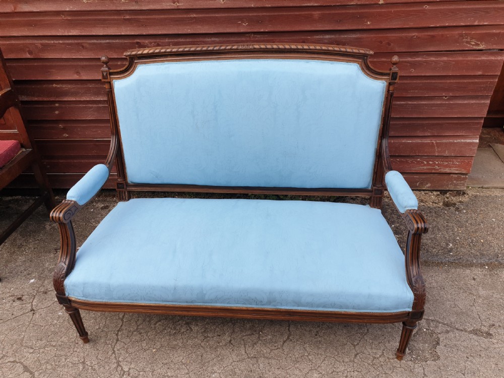 A French walnut two-seater hall settee featuring a carved wooden frame, fluted legs, padded armrests, and light blue upholstery. View III