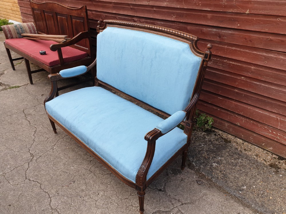 A French walnut two-seater hall settee featuring a carved wooden frame, fluted legs, padded armrests, and light blue upholstery. View V