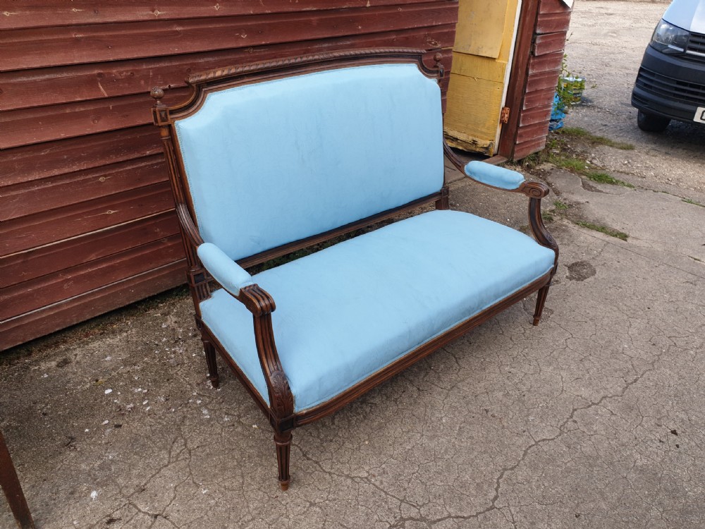 A French walnut two-seater hall settee featuring a carved wooden frame, fluted legs, padded armrests, and light blue upholstery. View VI