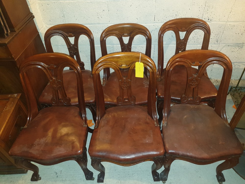 A set of six Victorian carved mahogany dining chairs featuring balloon backs, carved central splats, brown leather seats, and cabriole front legs. View V
