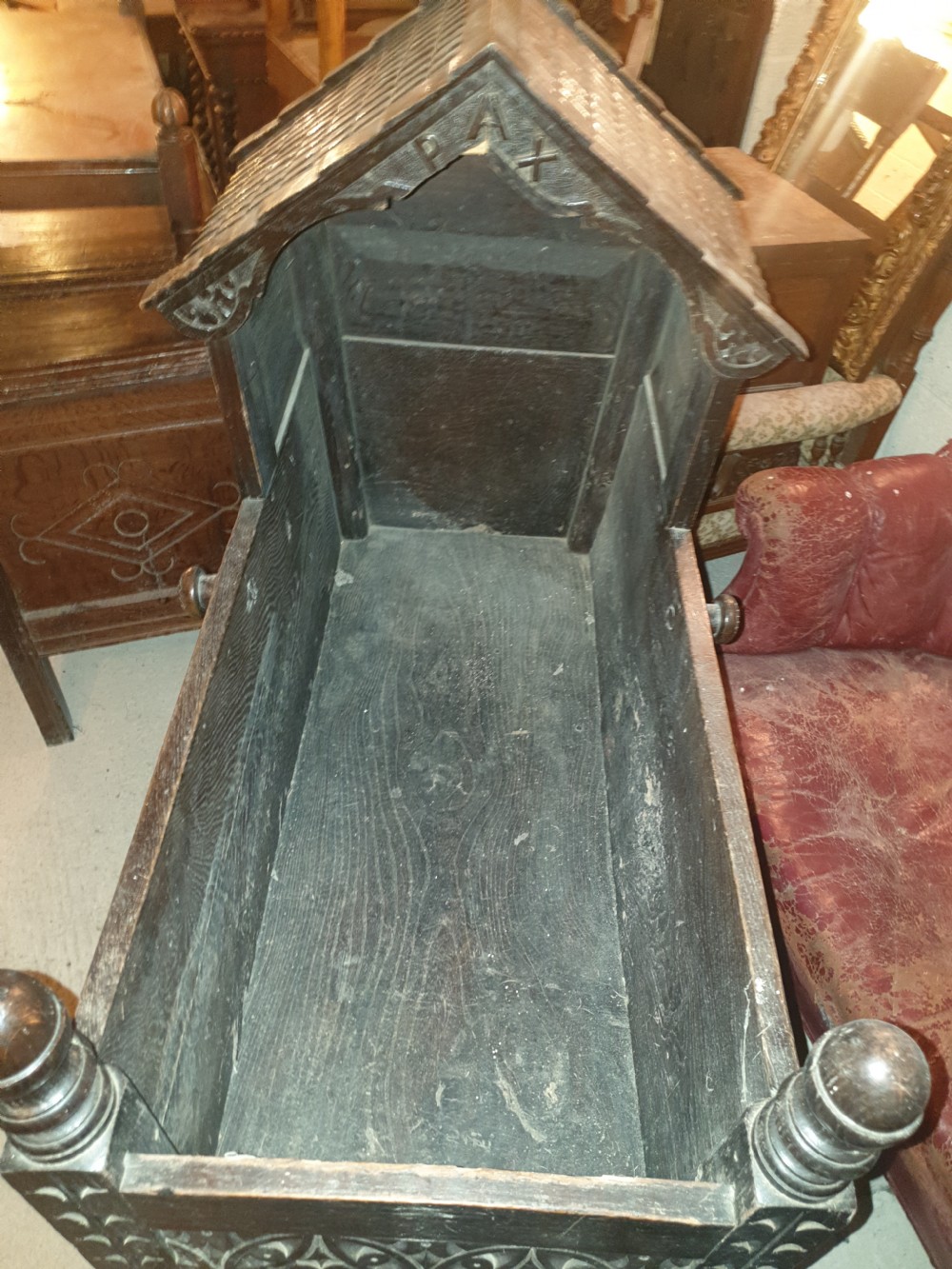 A dark carved oak Victorian rocking cradle featuring a tiled wooden hood, geometric floral carving, and turned finials. View III