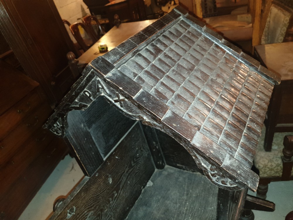 A dark carved oak Victorian rocking cradle featuring a tiled wooden hood, geometric floral carving, and turned finials. View V