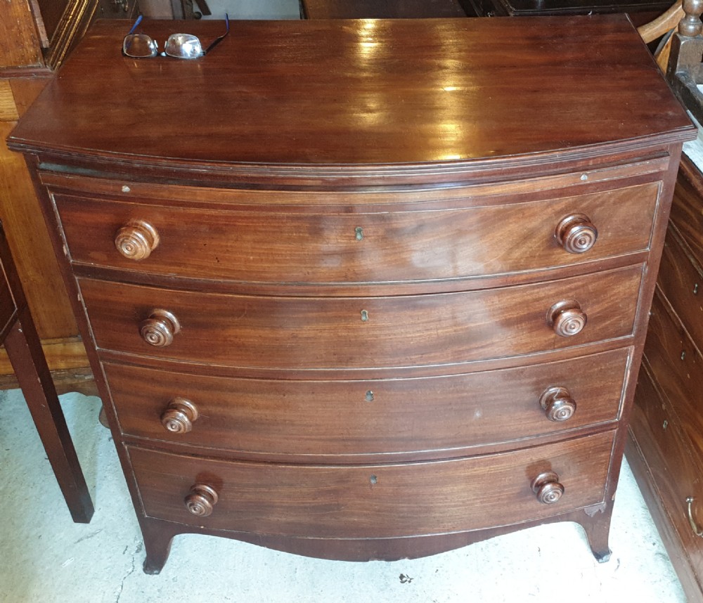 A Regency mahogany bowfront chest of drawers featuring four graduated drawers with turned wooden handles and a brushing slide, supported by splayed feet.