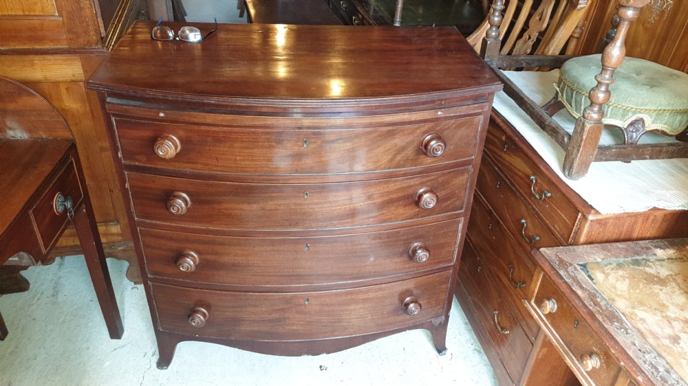 A Regency mahogany bowfront chest of drawers featuring four graduated drawers with turned wooden handles and a brushing slide, supported by splayed feet. View II
