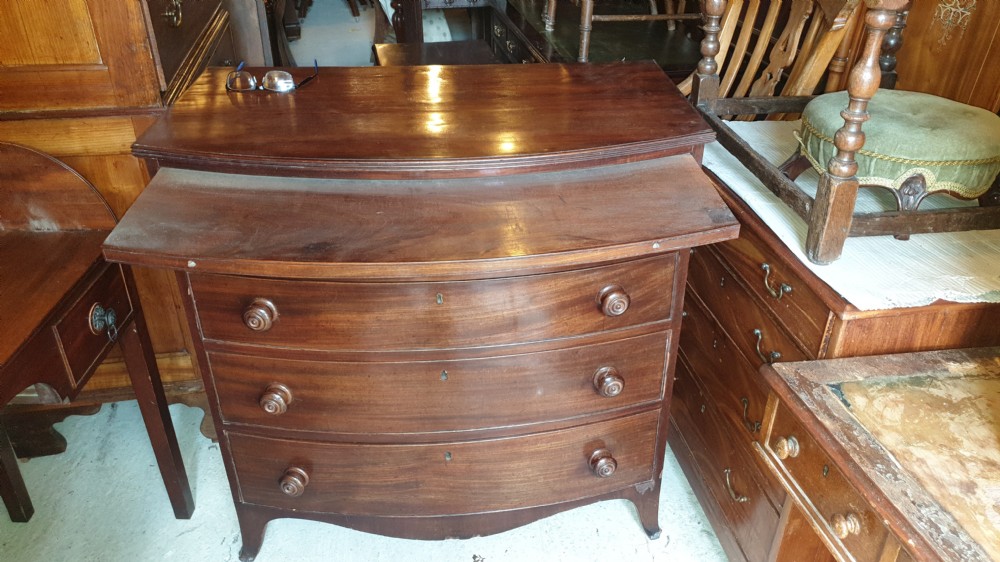 A Regency mahogany bowfront chest of drawers featuring four graduated drawers with turned wooden handles and a brushing slide, supported by splayed feet. View V