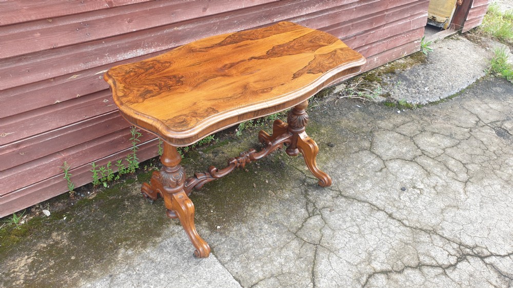 A Victorian rosewood side table featuring a serpentine-shaped top with distinct grain patterns, supported by turned end legs and a carved central stretcher. View II