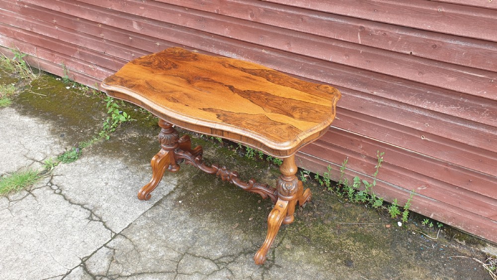 A Victorian rosewood side table featuring a serpentine-shaped top with distinct grain patterns, supported by turned end legs and a carved central stretcher. View III