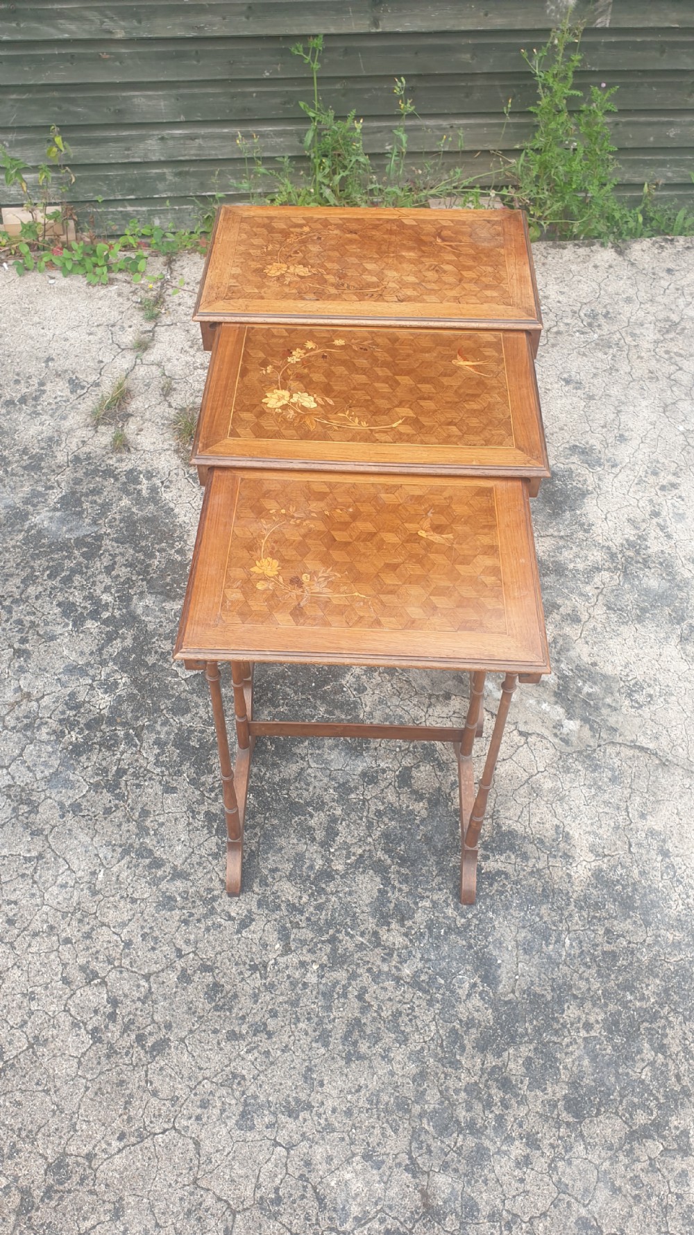 A set of three graduated wooden nesting tables featuring geometric parquetry tops inlaid with delicate floral and bird motifs.