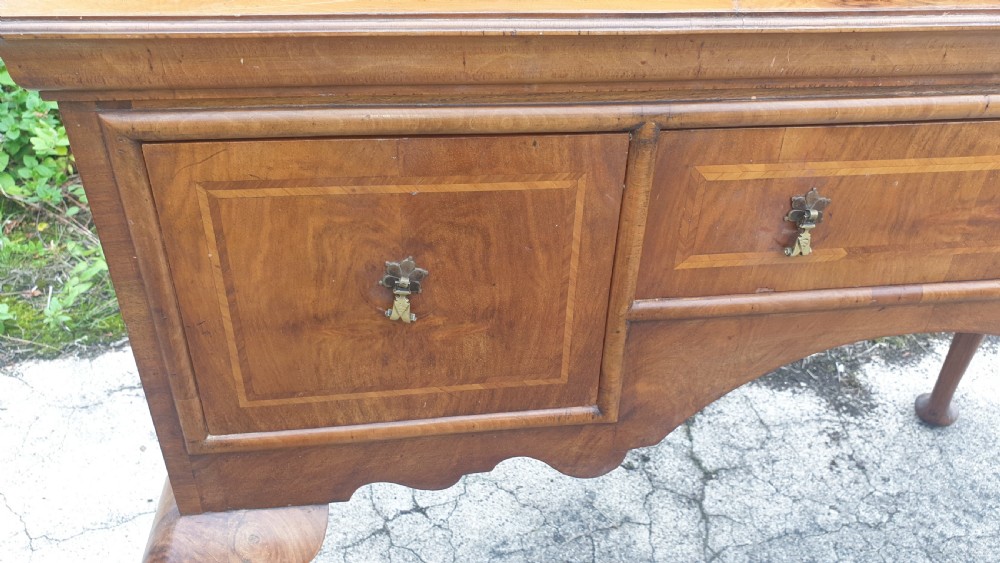 A Queen Anne style walnut side table featuring a figured veneer top, three drawers with brass handles, an arched apron, and four cabriole legs resting on pad feet. View II
