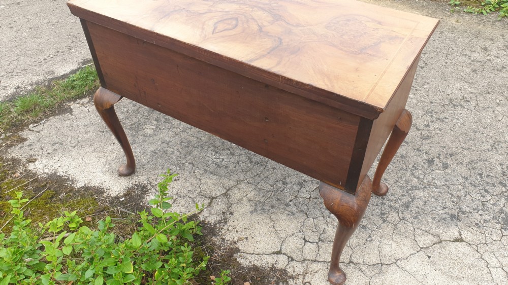 A Queen Anne style walnut side table featuring a figured veneer top, three drawers with brass handles, an arched apron, and four cabriole legs resting on pad feet. View V