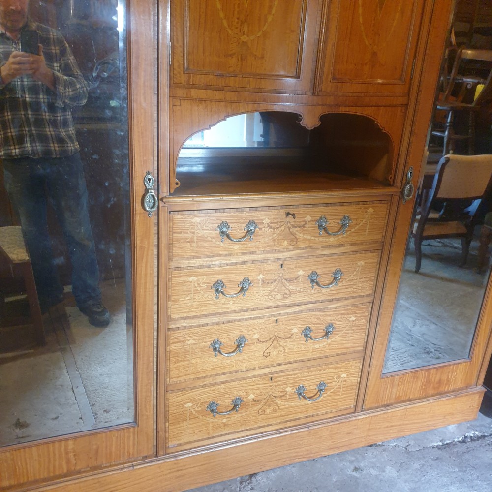 An antique three-section satinwood wardrobe featuring inlaid urn marquetry, central drawers, and two tall outer doors with arched mirrors. View VIII
