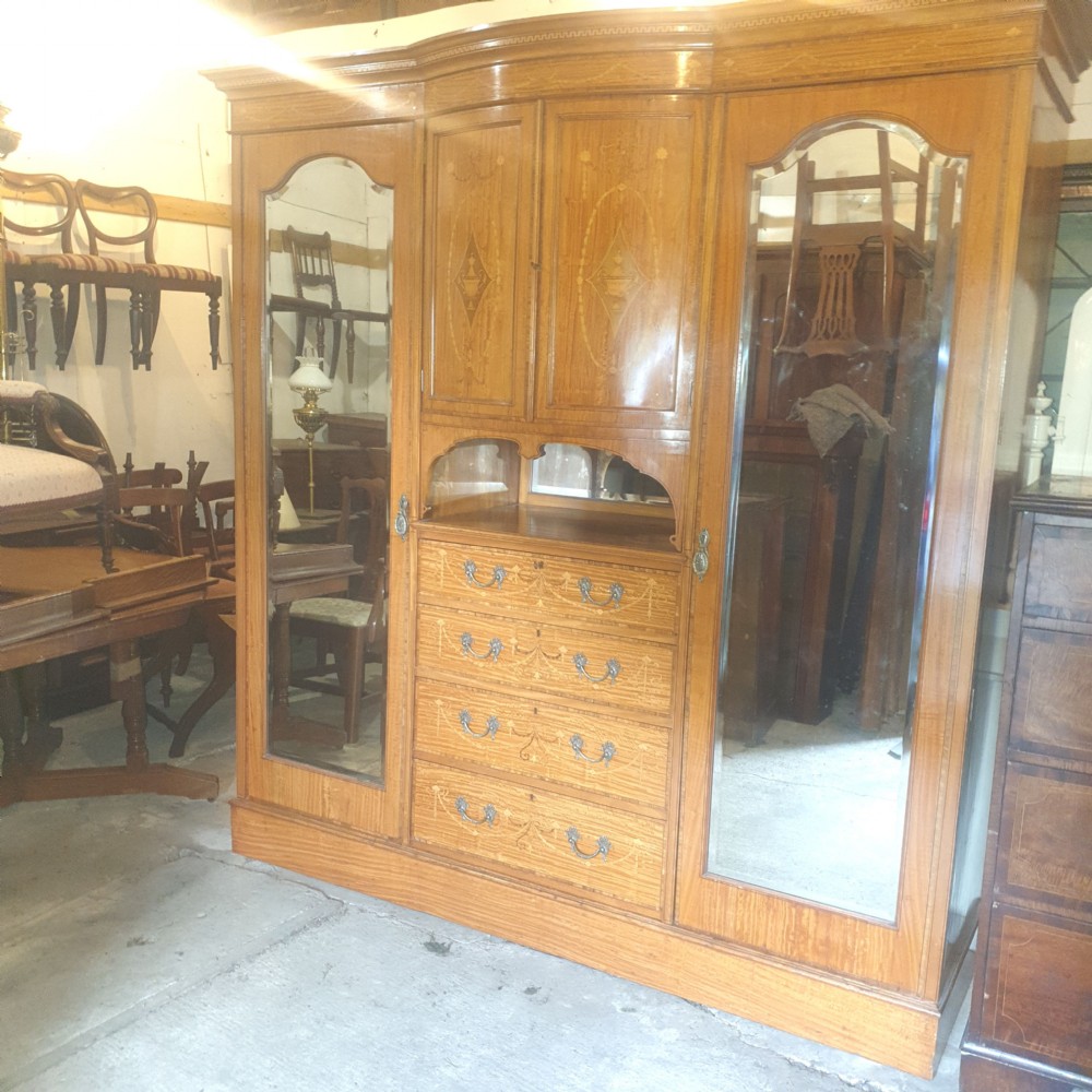 An antique three-section satinwood wardrobe featuring inlaid urn marquetry, central drawers, and two tall outer doors with arched mirrors. View IX