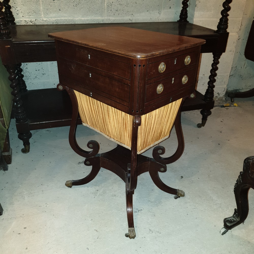 An antique Regency mahogany sewing table featuring inlaid drawers, a pleated fabric work basket, and swept legs with brass castors. View II