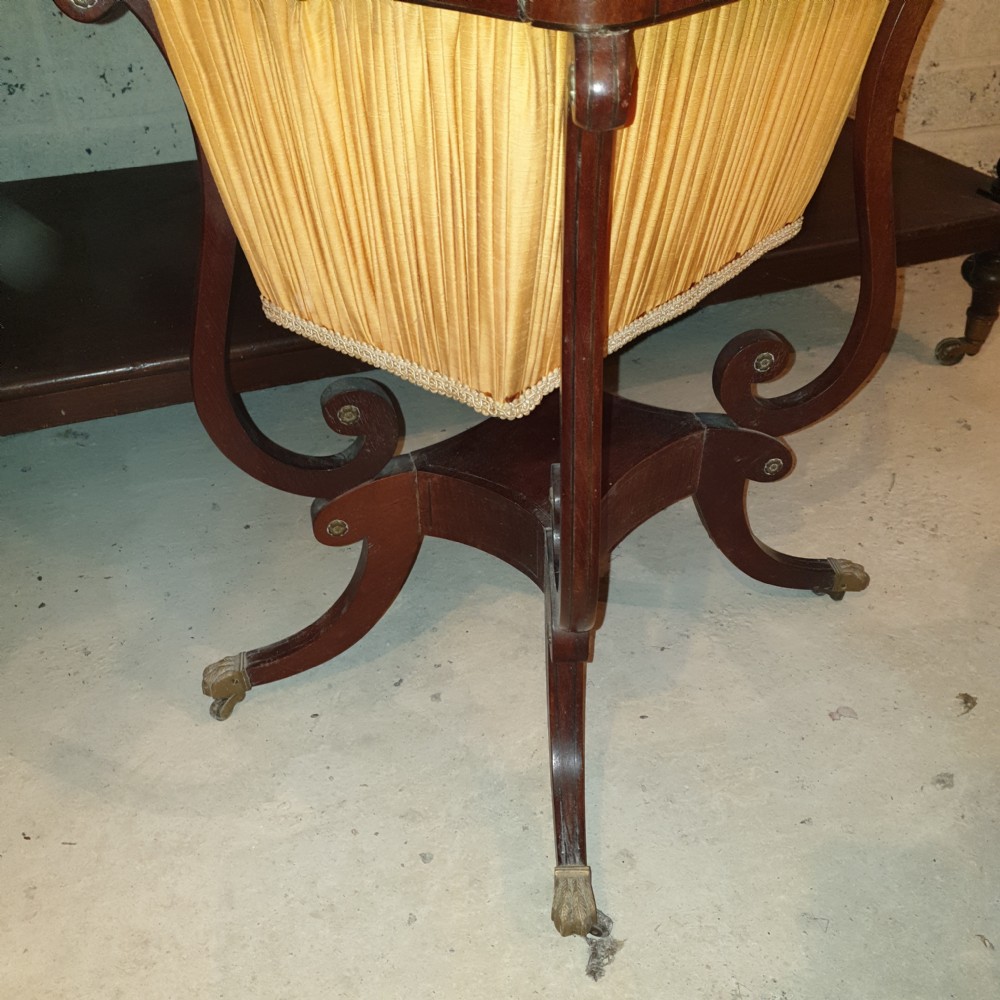 An antique Regency mahogany sewing table featuring inlaid drawers, a pleated fabric work basket, and swept legs with brass castors. View III