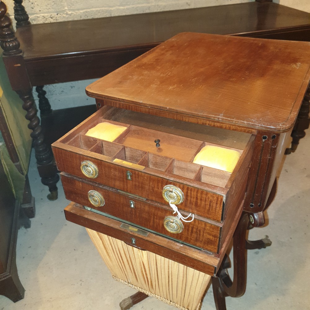 An antique Regency mahogany sewing table featuring inlaid drawers, a pleated fabric work basket, and swept legs with brass castors. View VI