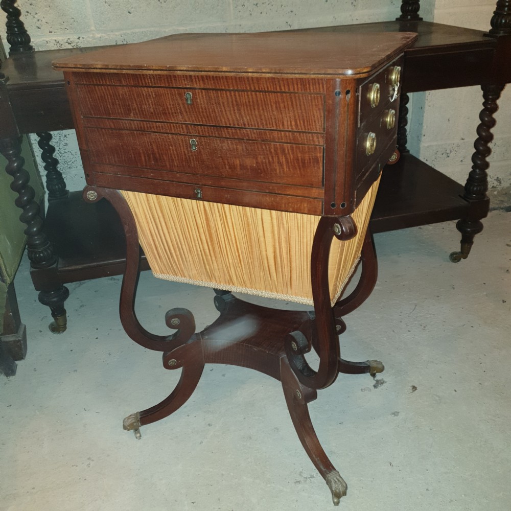 An antique Regency mahogany sewing table featuring inlaid drawers, a pleated fabric work basket, and swept legs with brass castors. View VIII