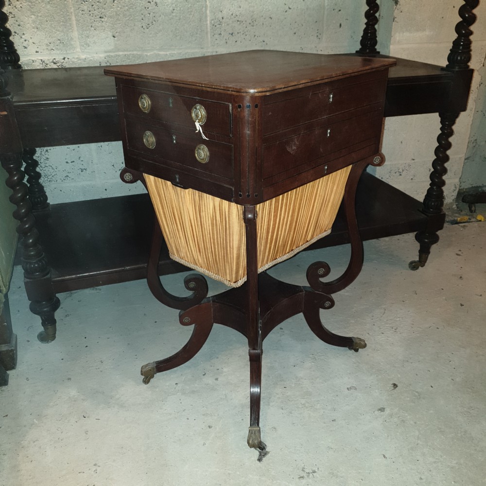 An antique Regency mahogany sewing table featuring inlaid drawers, a pleated fabric work basket, and swept legs with brass castors. View IX