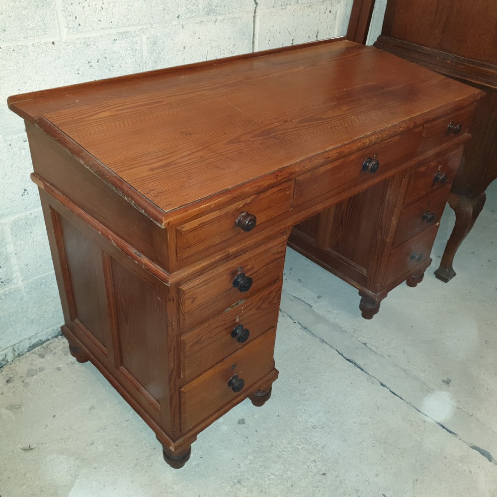 A late Victorian pitch pine pedestal desk featuring nine drawers with turned wooden handles, a low rear gallery rail, and turned feet.