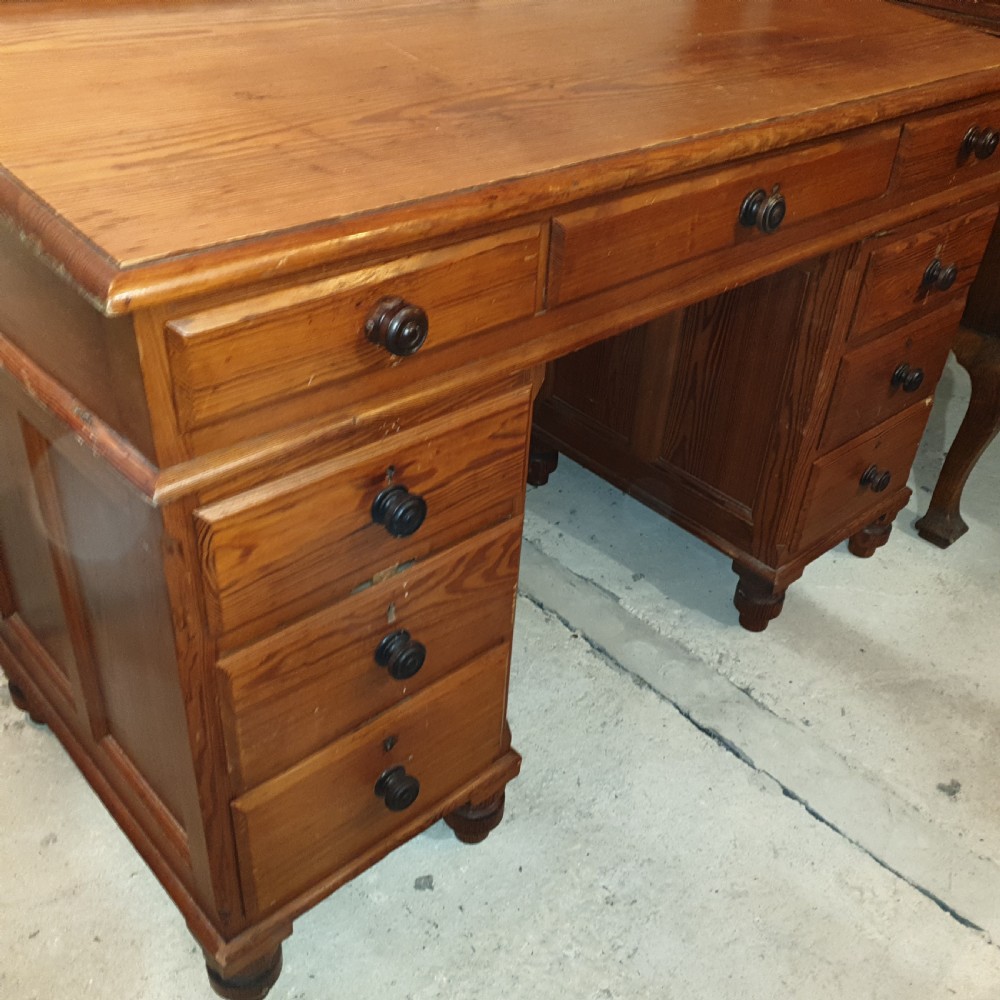 A late Victorian pitch pine pedestal desk featuring nine drawers with turned wooden handles, a low rear gallery rail, and turned feet. View II
