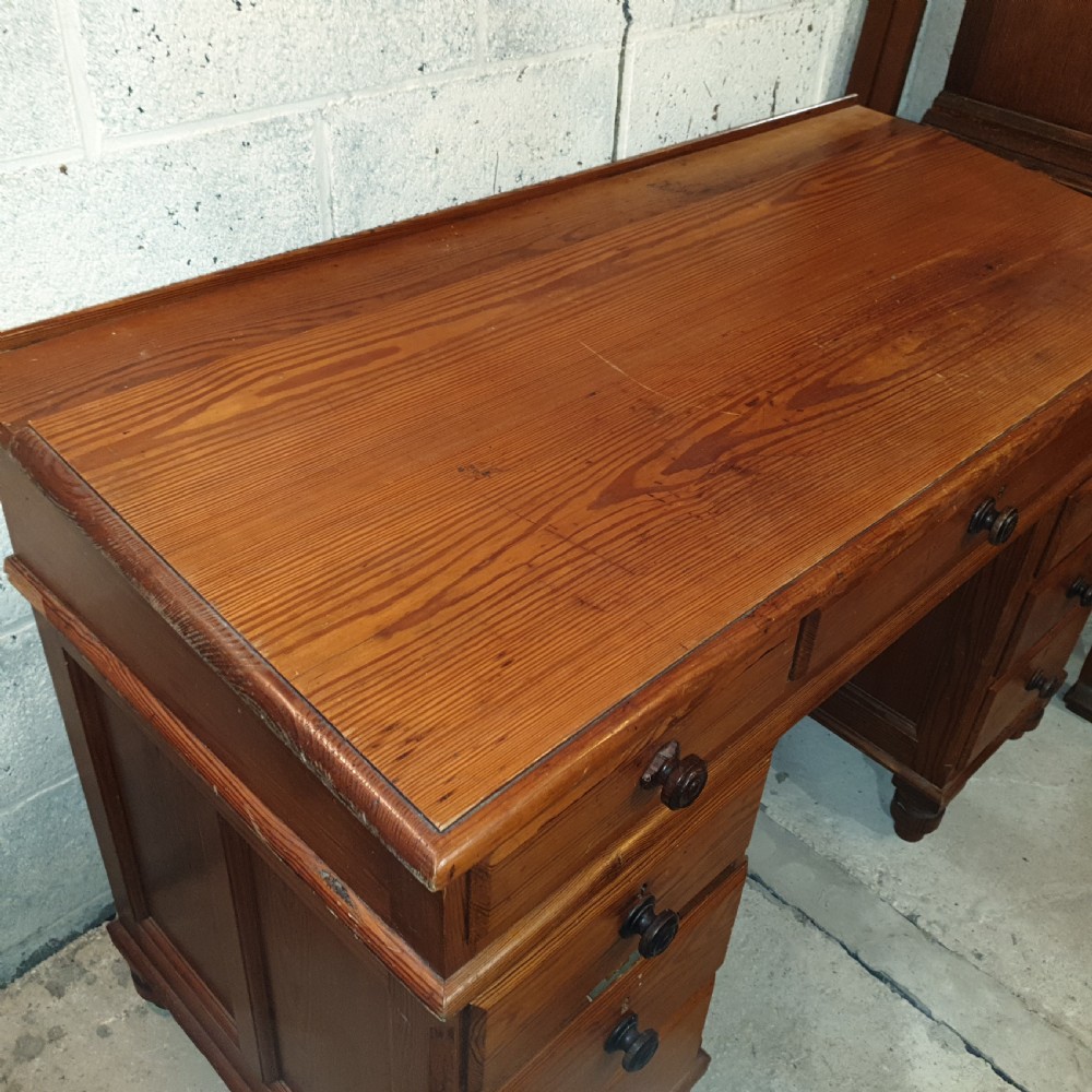 A late Victorian pitch pine pedestal desk featuring nine drawers with turned wooden handles, a low rear gallery rail, and turned feet. View III