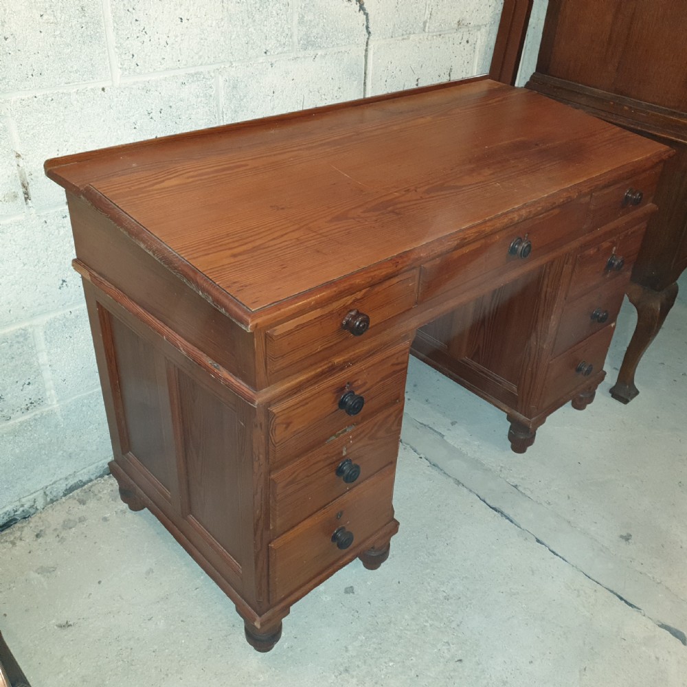 A late Victorian pitch pine pedestal desk featuring nine drawers with turned wooden handles, a low rear gallery rail, and turned feet. View V