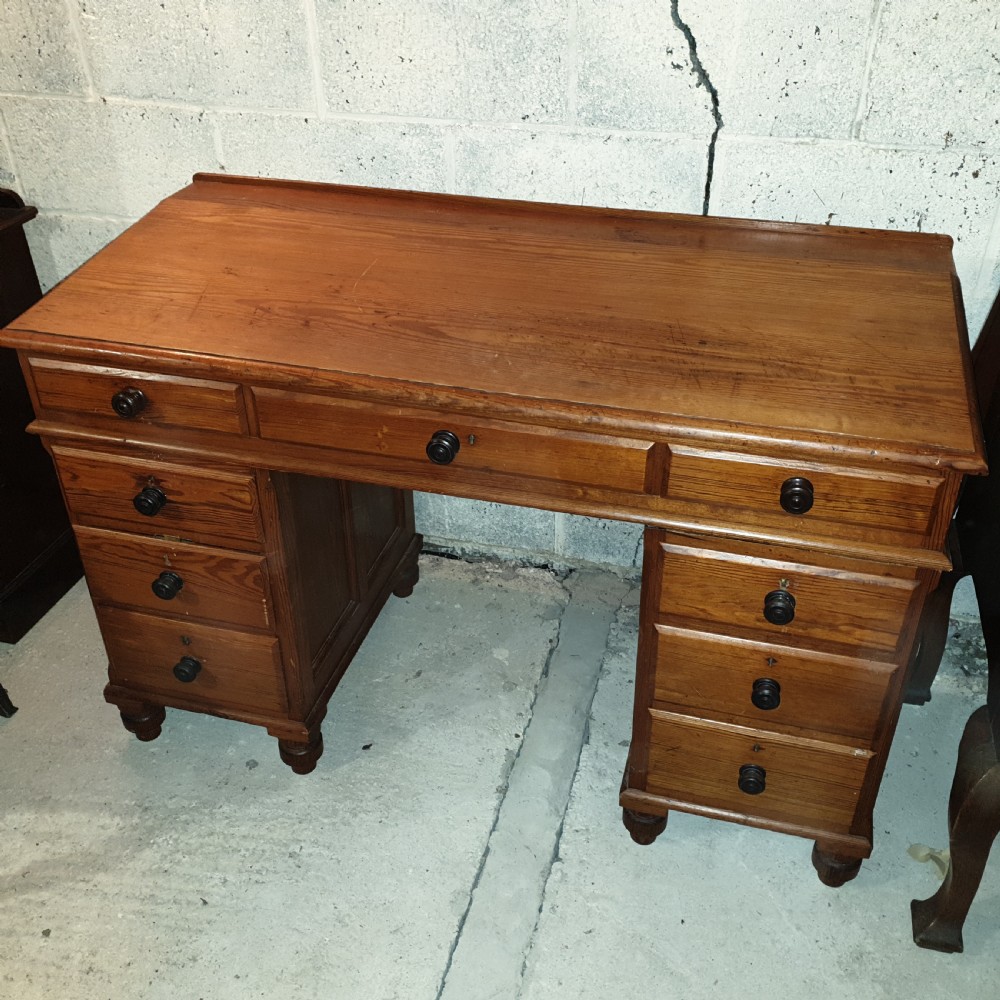 A late Victorian pitch pine pedestal desk featuring nine drawers with turned wooden handles, a low rear gallery rail, and turned feet. View VI