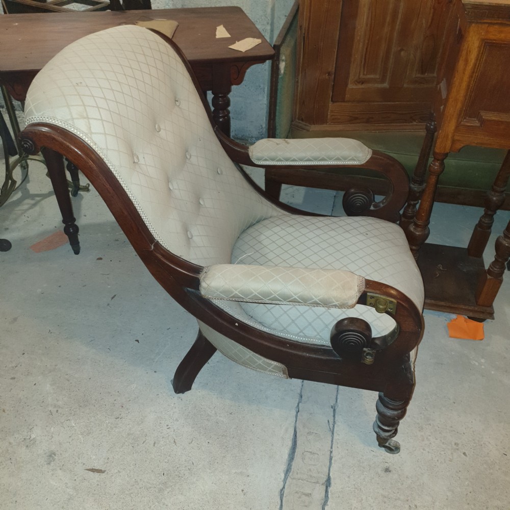 Early Victorian mahogany library armchair featuring button-tufted light upholstery, scrolled padded arms, turned front legs, and brass castors. View II