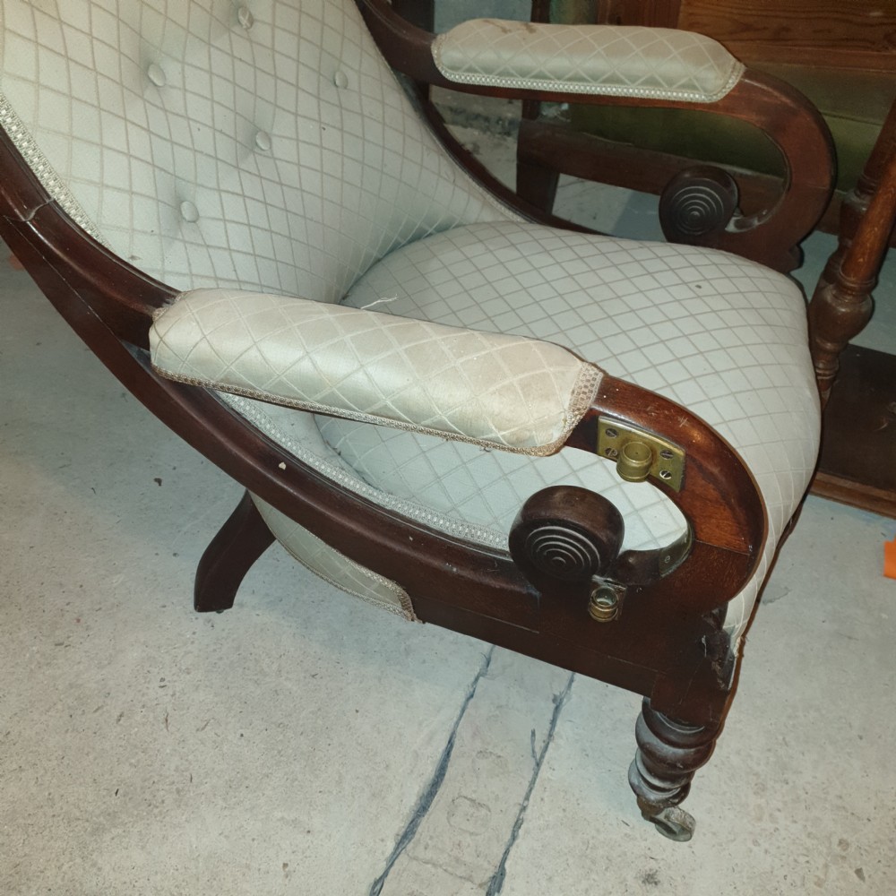 Early Victorian mahogany library armchair featuring button-tufted light upholstery, scrolled padded arms, turned front legs, and brass castors. View IV