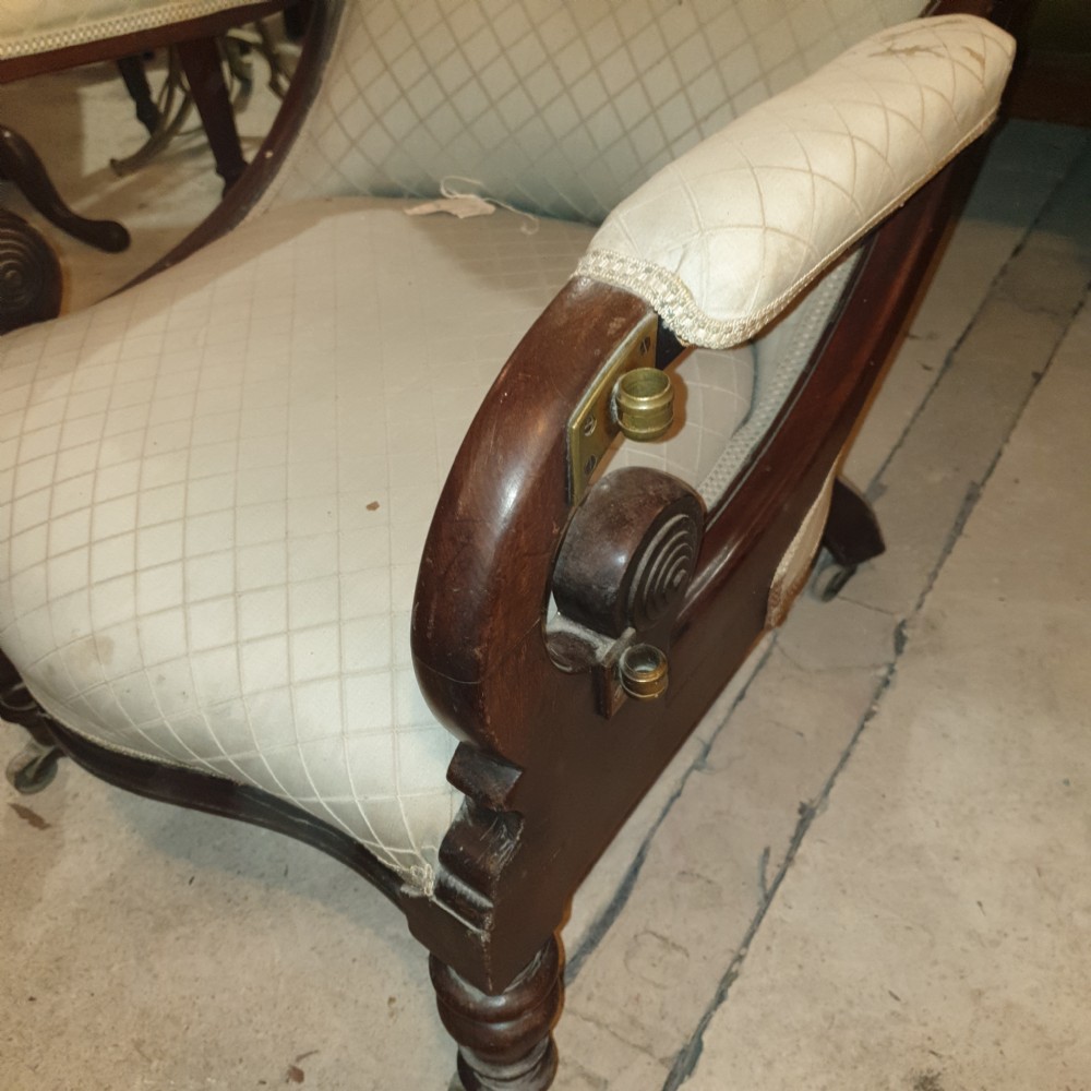 Early Victorian mahogany library armchair featuring button-tufted light upholstery, scrolled padded arms, turned front legs, and brass castors. View V
