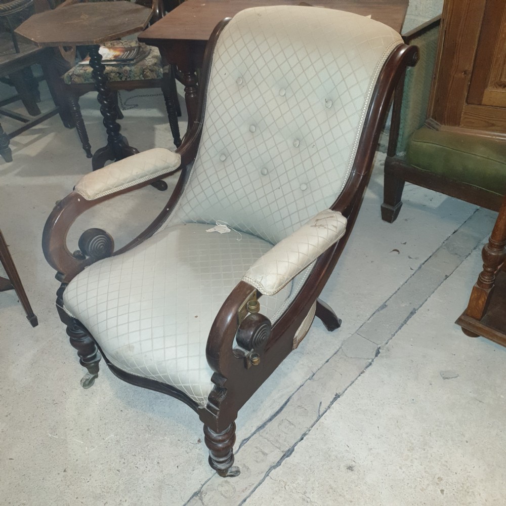 Early Victorian mahogany library armchair featuring button-tufted light upholstery, scrolled padded arms, turned front legs, and brass castors. View VI