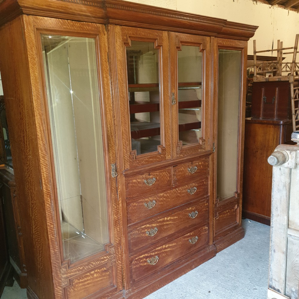 An Edwardian satinwood triple wardrobe featuring mirrored side doors, a central upper compartment, five drawers, and a stepped cornice top. View II