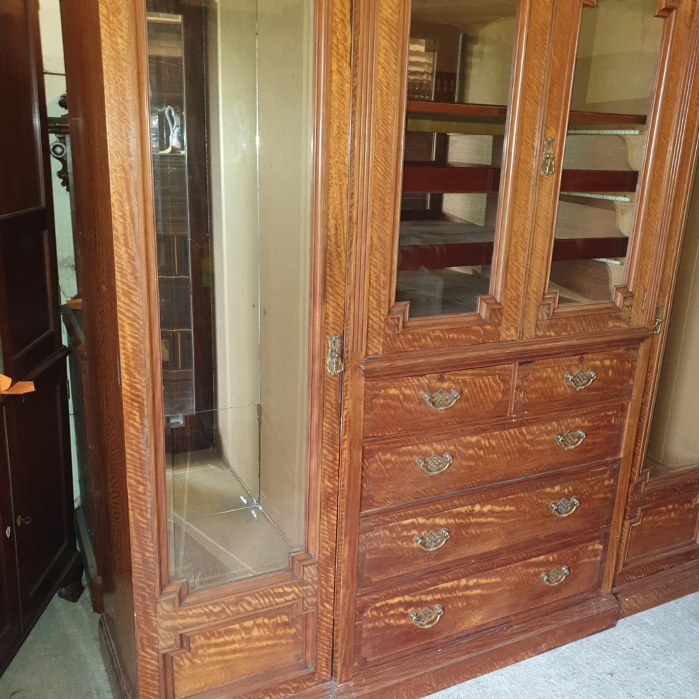 An Edwardian satinwood triple wardrobe featuring mirrored side doors, a central upper compartment, five drawers, and a stepped cornice top. View IV