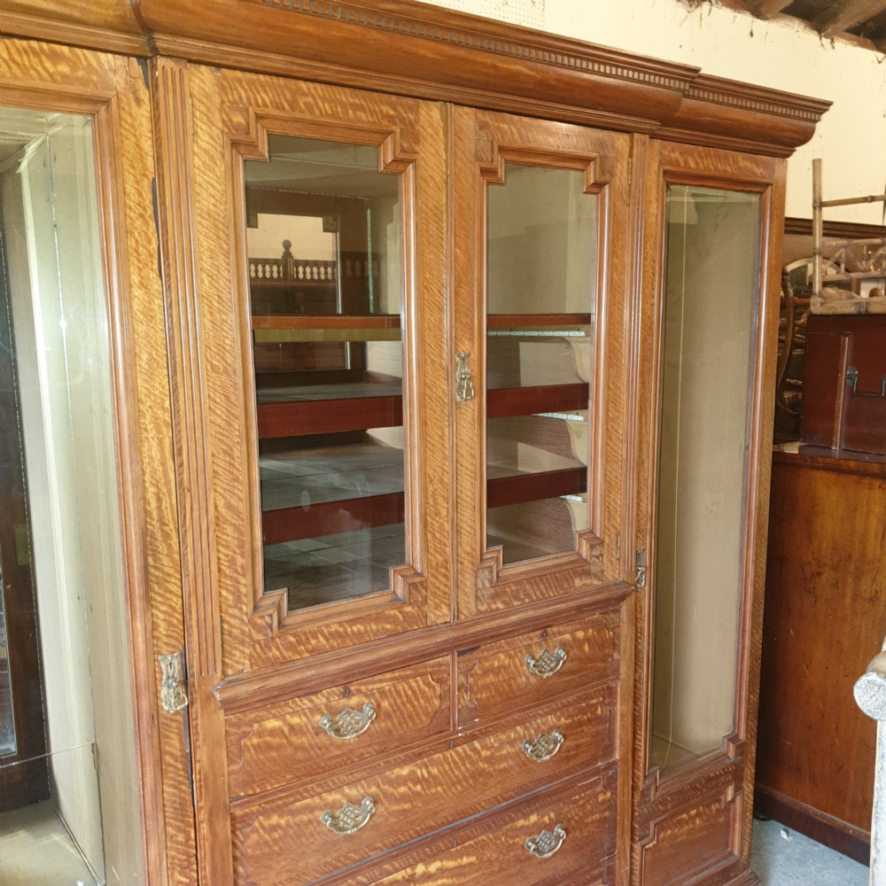 An Edwardian satinwood triple wardrobe featuring mirrored side doors, a central upper compartment, five drawers, and a stepped cornice top. View V